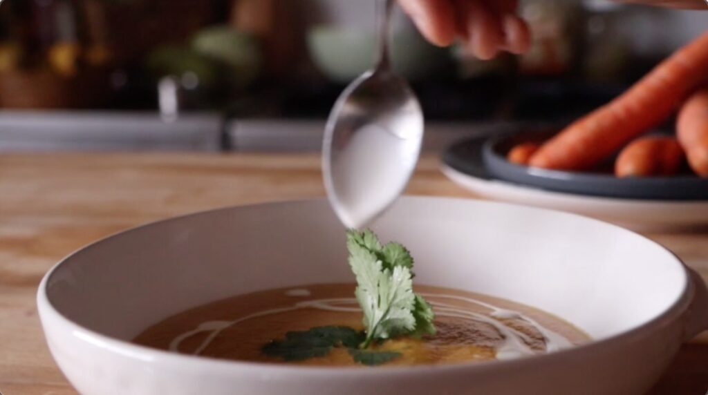 spoon drizzles cream on sweet potato soup