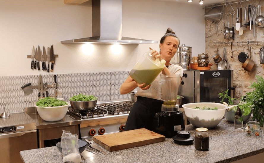 woman pouring light green liquid from a canister into a high-speed blender in kitchen