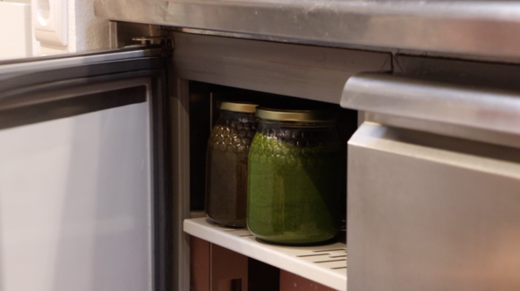 two glass jars filled with green paste standing in a fridge