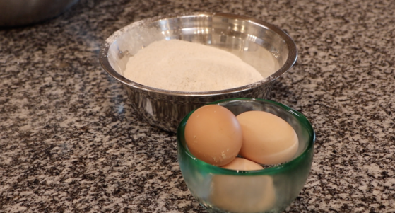 small glass bowl with three eggs and slightly bigger metal bowl with white flour