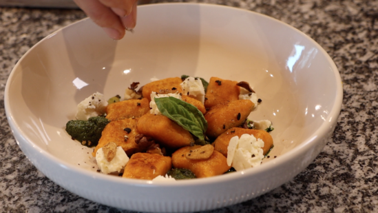 black pepper being sprinkled over a plate with orange gnocchi