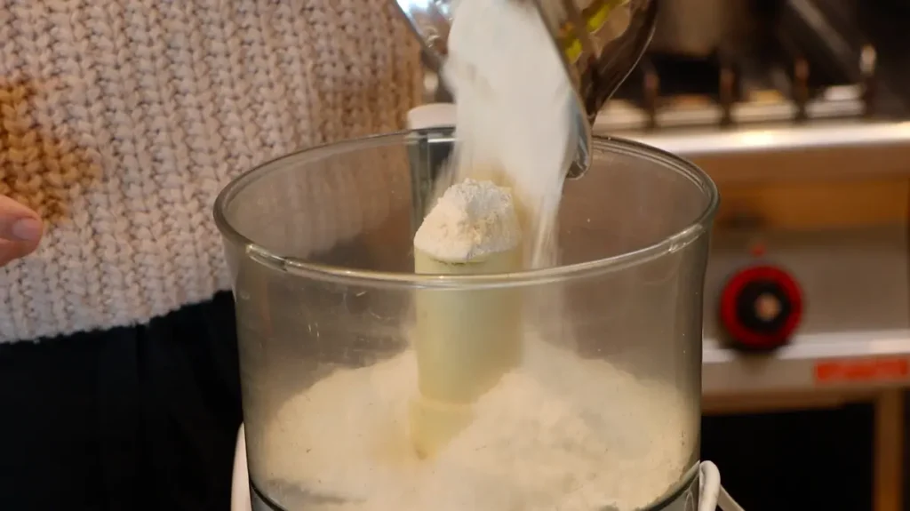 white powder falling into food processor from silver bowl