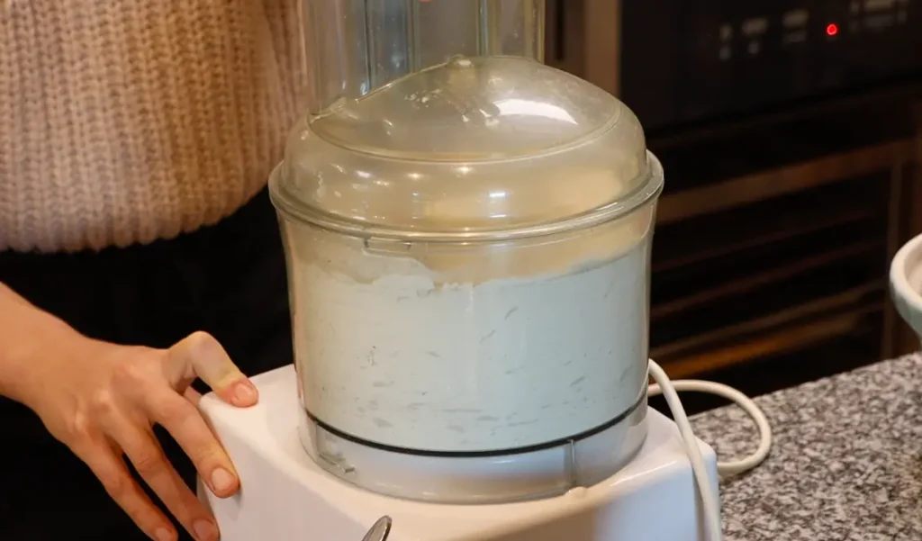 closed food processor with white powdery substance and hand resting