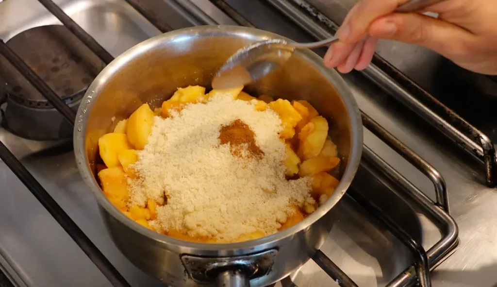 top view of pot on stove, fruit inside, spoon, brown powder and sand like substance