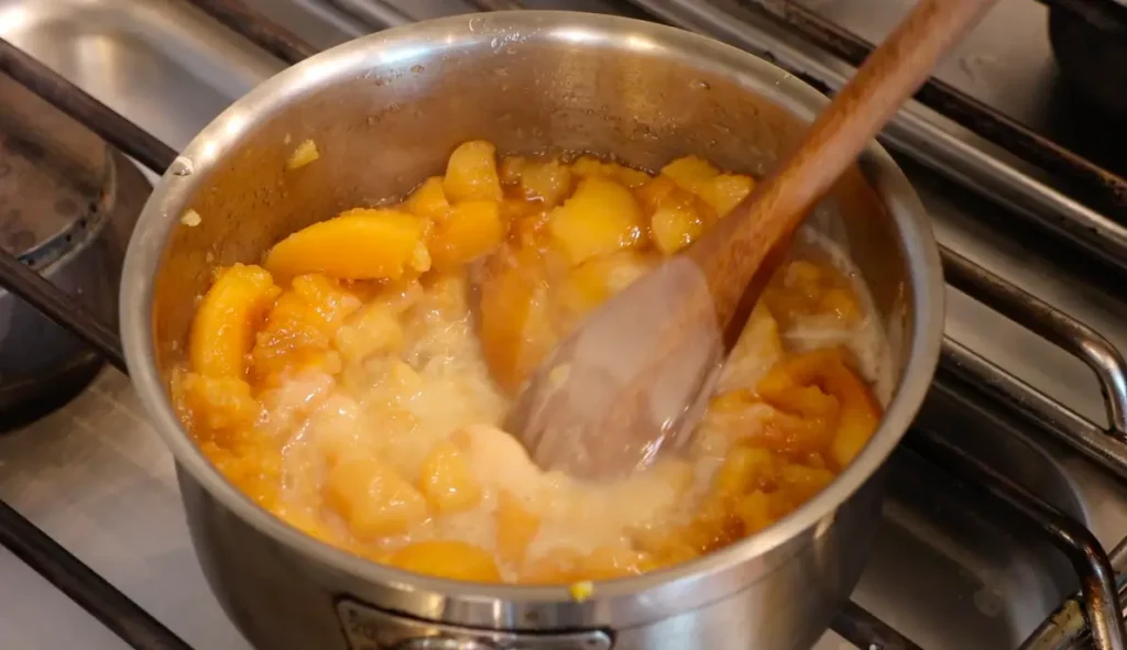 wooden spoon inside a pot wit yellow fruits and white liquid