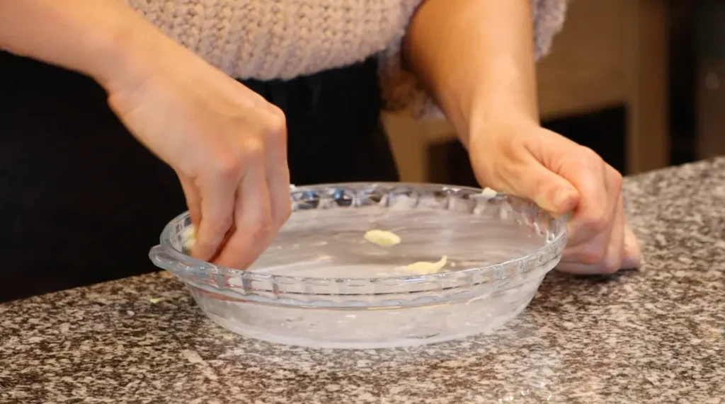 glass pie dish being covered with butter