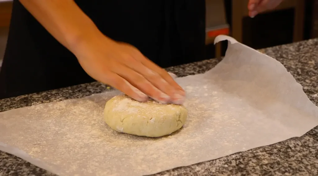 dough disk on white paper, hand spreading out white powder