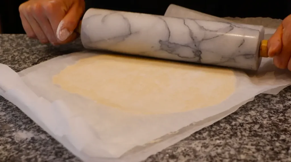 light yellow dough between two sheets of paper, black and white marbled rolling pin