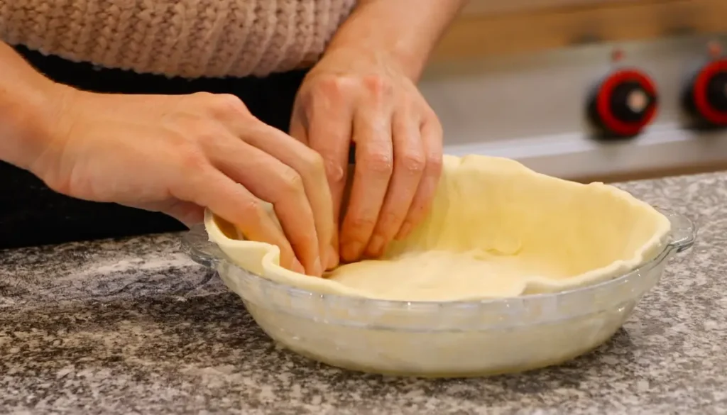 two hands pressing dough sheet into glass pie dish