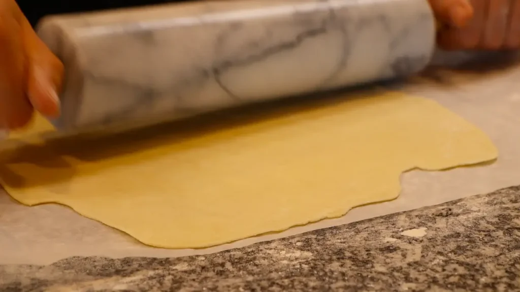 thin sheet of dough on white paper, marbled black and white rolling pin