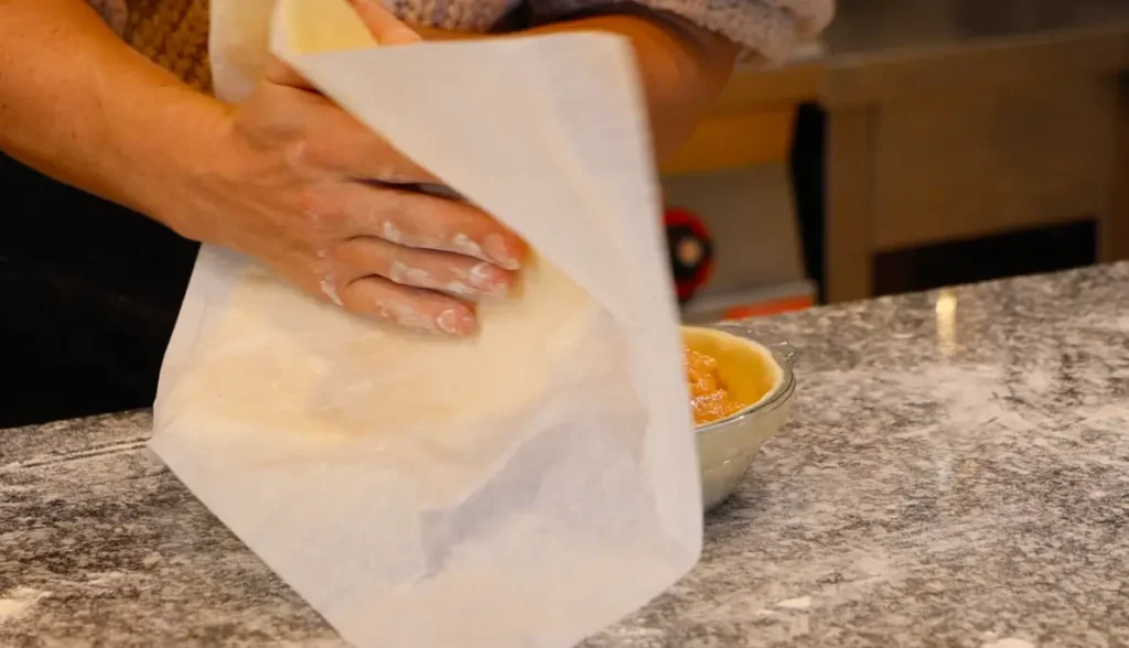 dough sheet attached to white paper, two hands laying dough onto pie