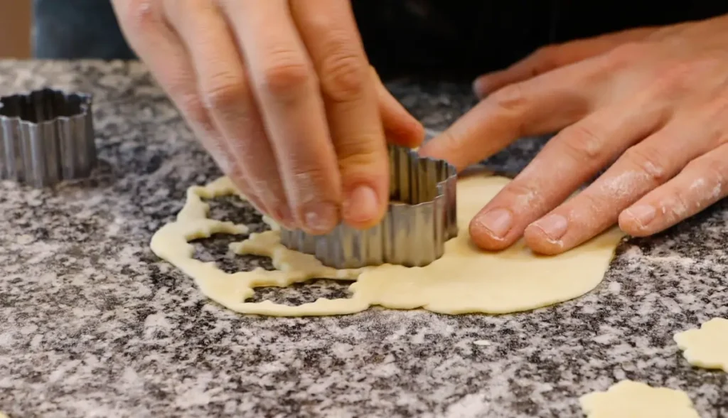 metal cookie cutter cutting floral shapes from dough sheet