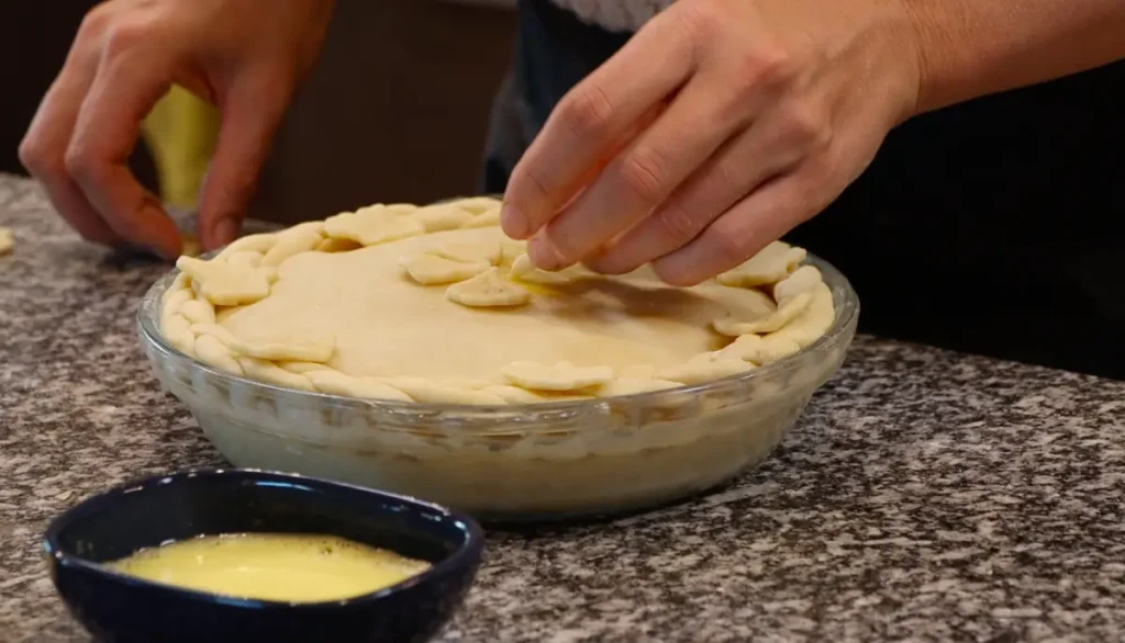 hand placing floral shapes from dough onto pie