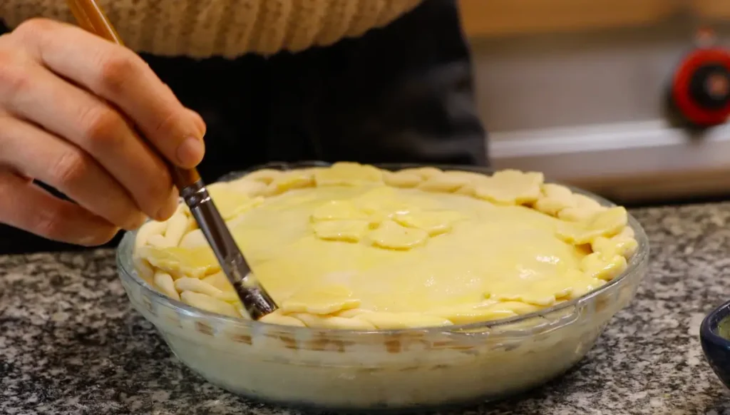 small brush brushing yellow liquid onto decorated pie