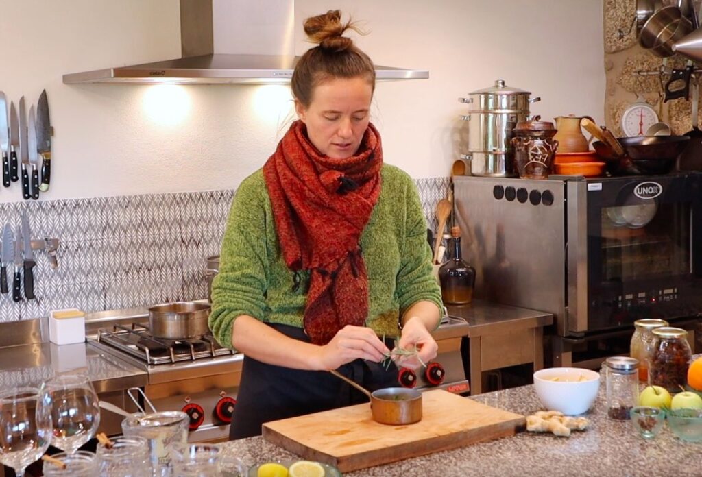 woman in kitchen adding fresh herbs to small copper pot