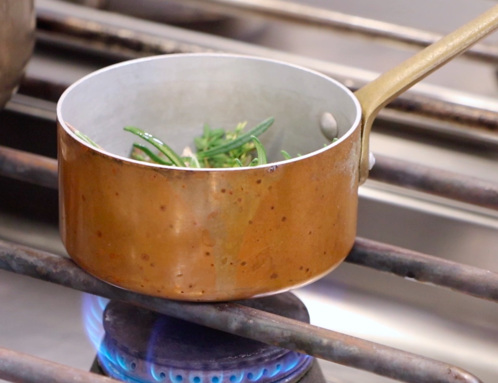 small bronze pot on gas stove, green herbs inside