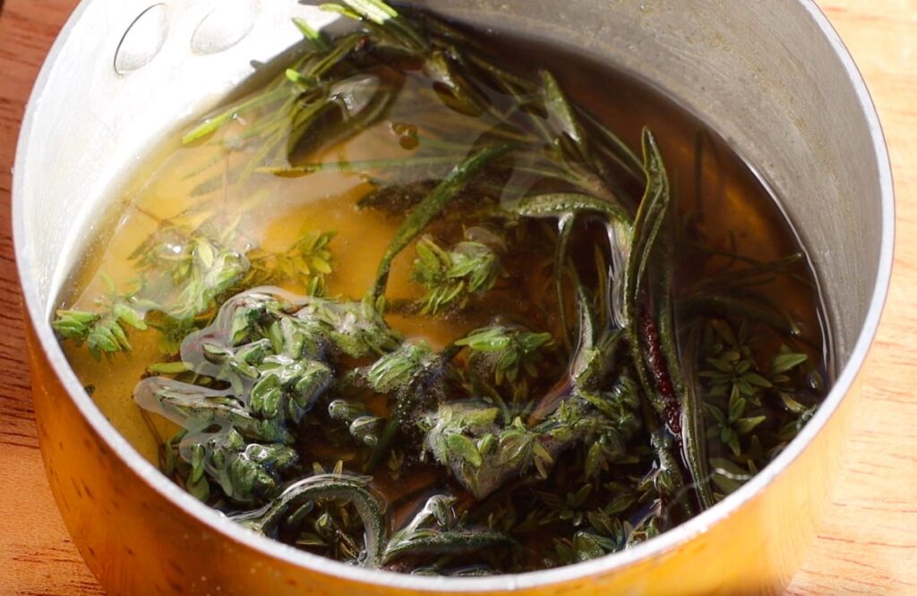 two types of green herbs in small pt with golden liquid