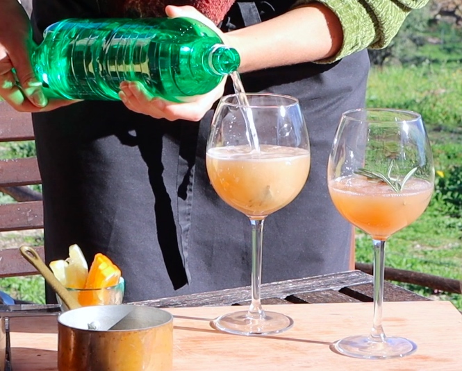 two wine glasses with dark yellow liquid, water being poured from green bottle into glass