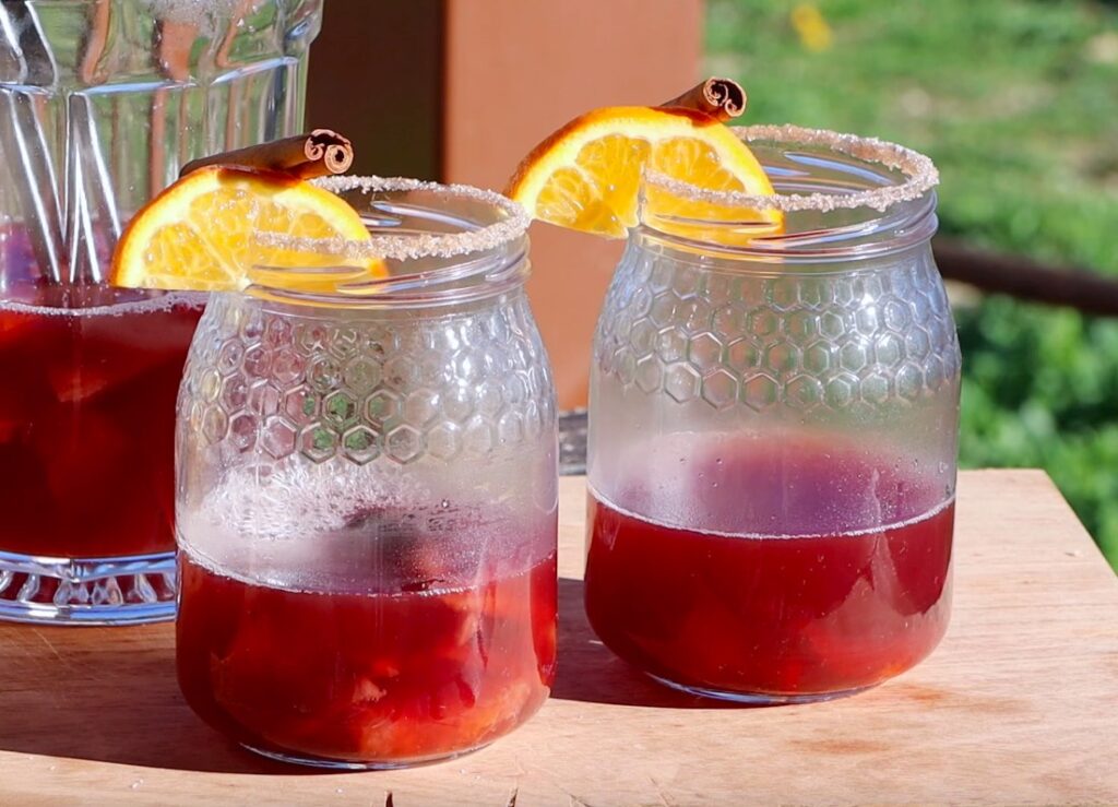 two big jars, filled one third with deep red liquid, sugared edge, orange slice and cinnamon stick