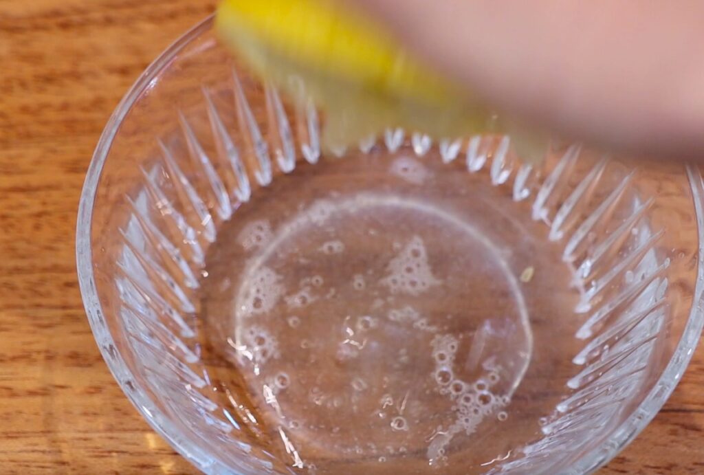 glass bowl with almost transparent liquid, blurry hand holding half a lemon