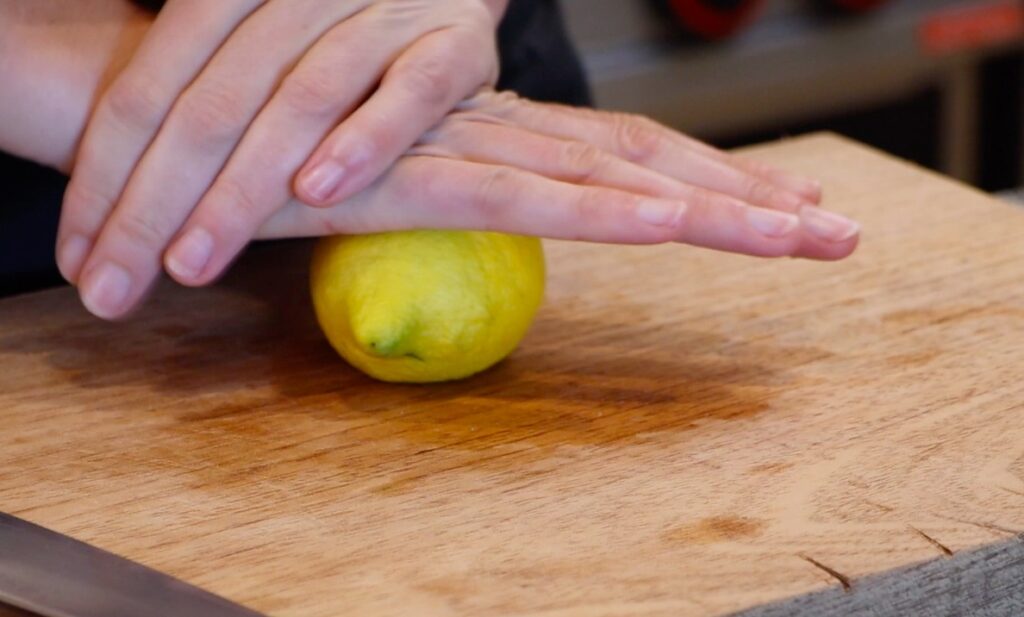 two hands rolling lemon on wooden cutting board