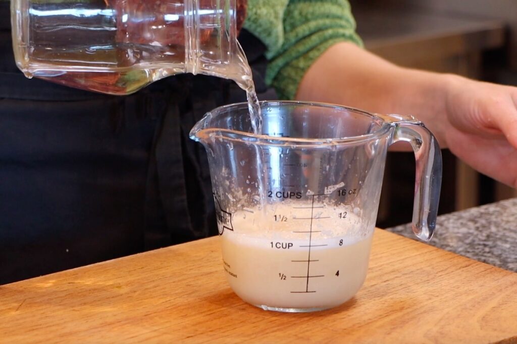 water being poured from glass jug into glass measuring cup with cream liquid