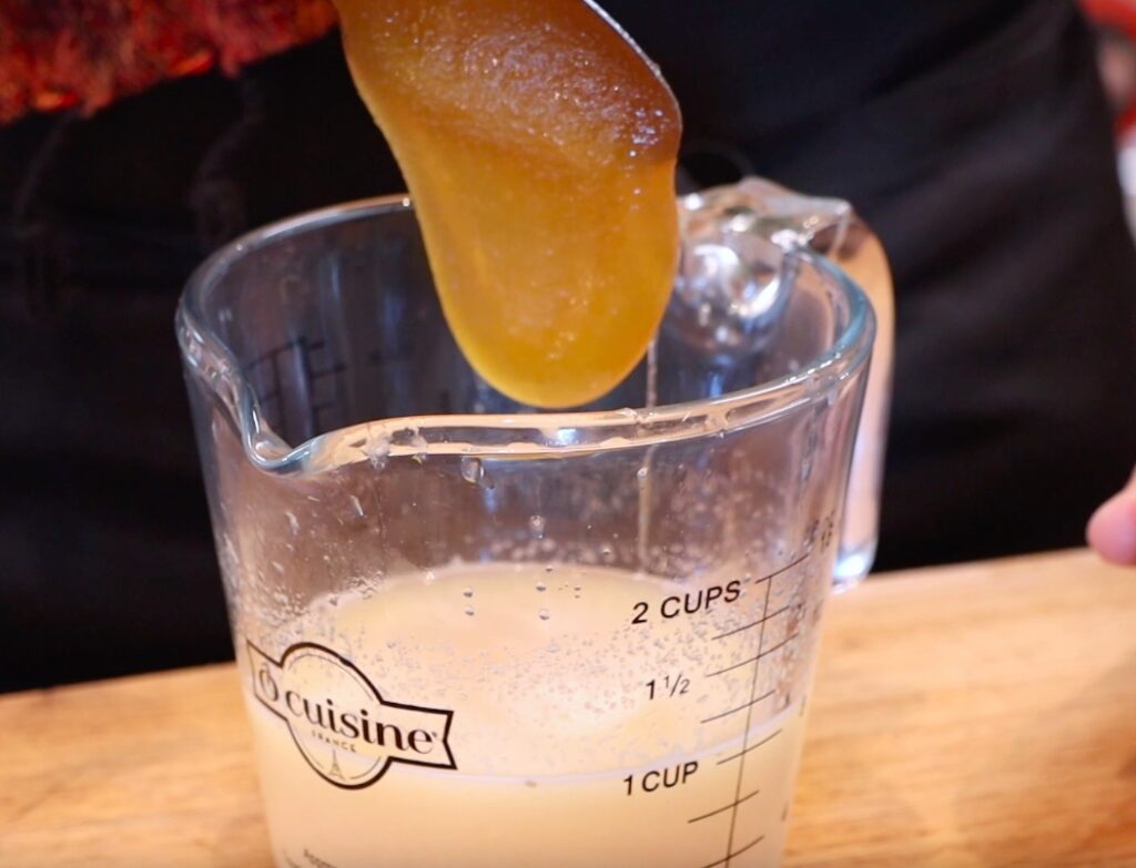 golden-brown grey substance dropping into glass measuring cup