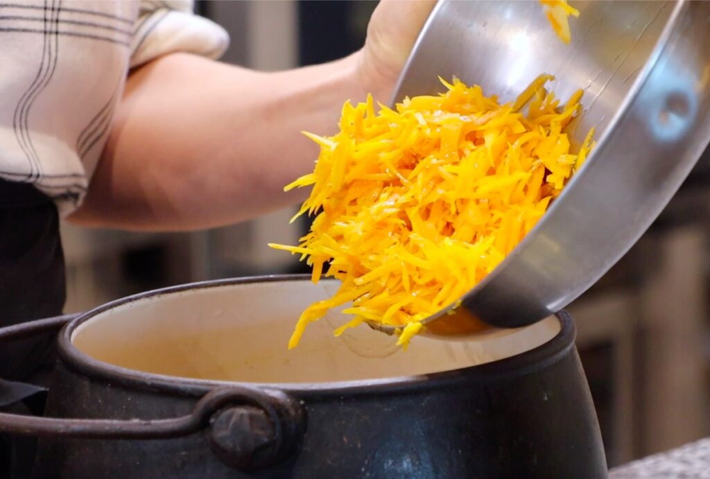 orange peels dropping into black and white pot from metal bowl