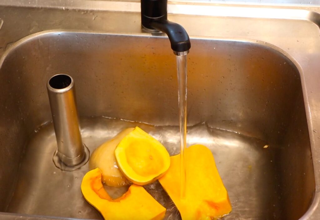 big pieces of light orange pumpkin in sink, water running