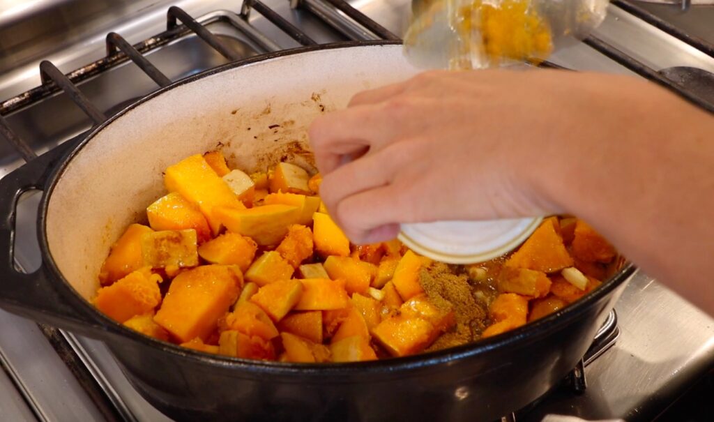 oval pot with pumpkin, hand holding little bowl upside down, light brown powder in pot on top of pumpkin