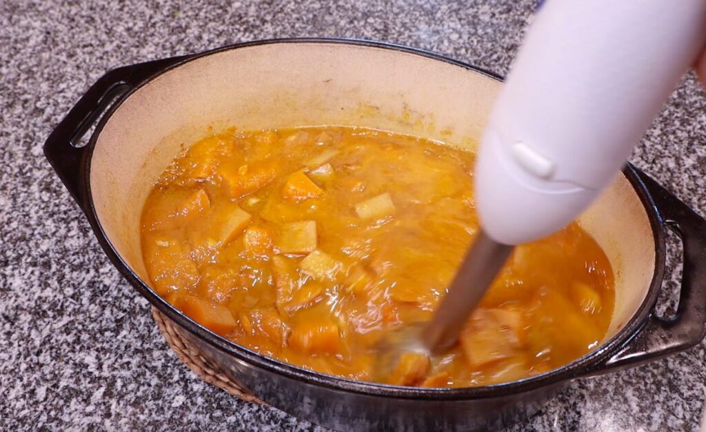 chunky orange liquid in oval pot, white hand blender inside