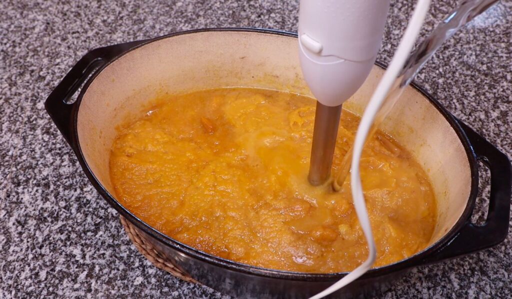 oval pot, blended orange soup, water pouring into pot, white hand blender