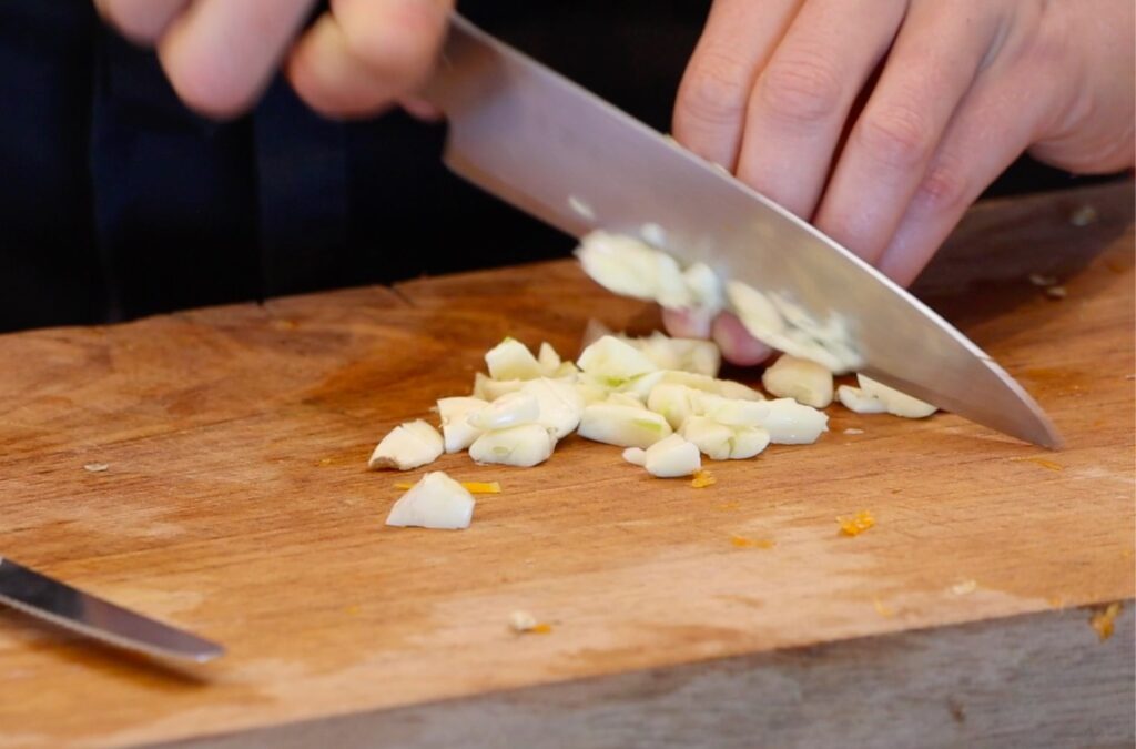 garlic being chopped on wooden board with big knife