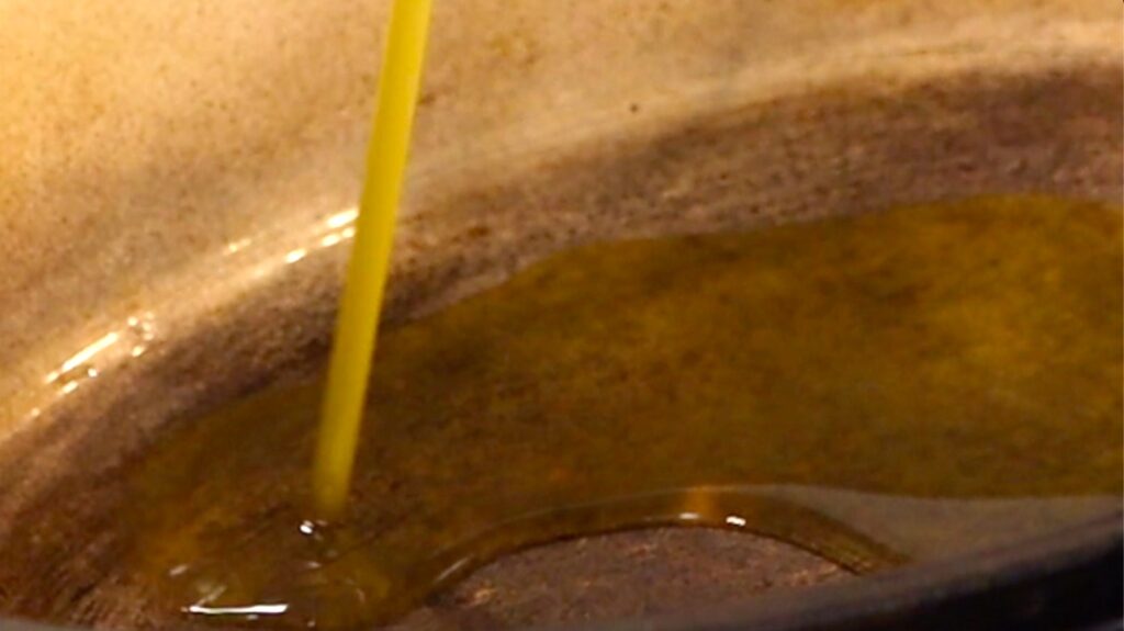 close-up of light olive-green liquid pouring into metal pot