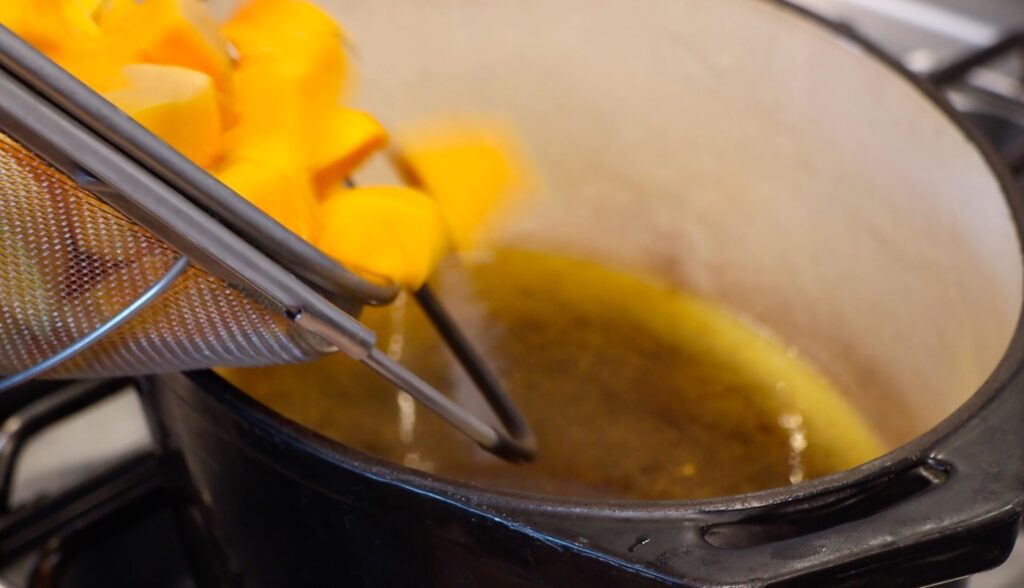 close-up of pumpkin cubes falling into pot, bottom covered with olive oil