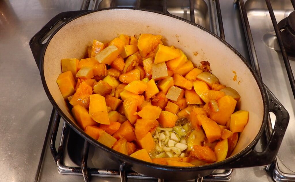 oval pot on stove, pumpkin pieces, chopped garlic in one spot, bubbling in light green liquid