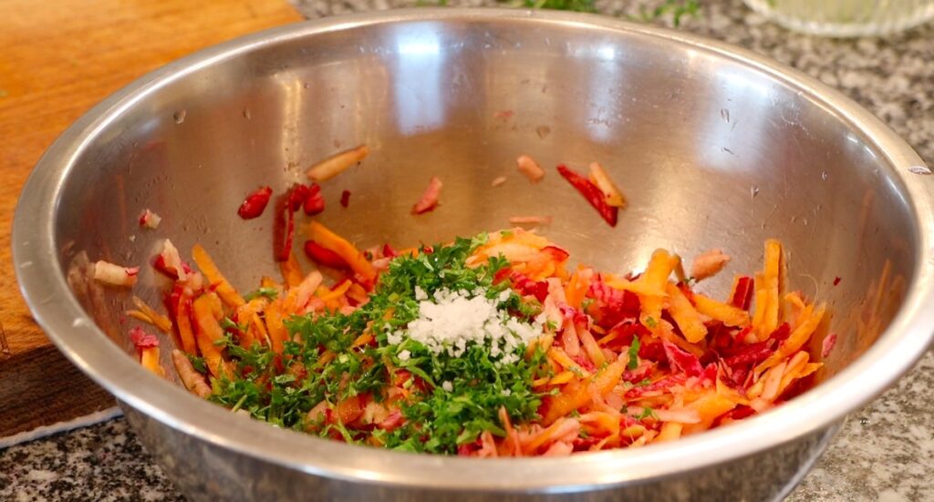 metal bowl with grated pink beetroot, apple and carrots, topped with finely chopped fresh green herbs, coarse salt