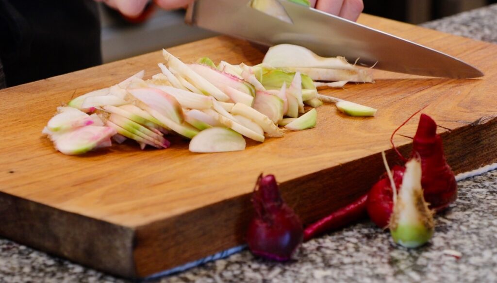 white root vegetable being sliced with big knife on wooden board