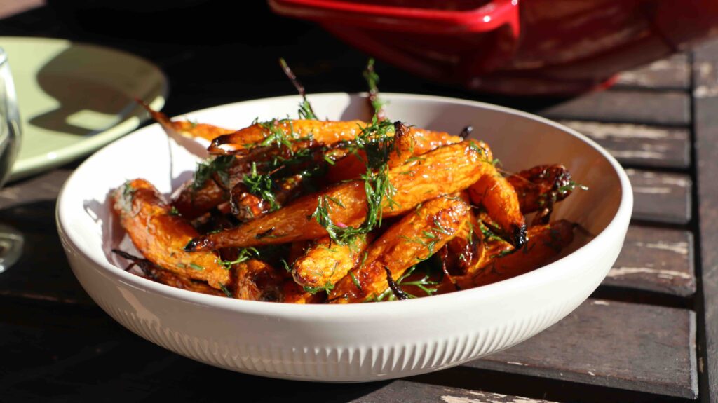 white bowl with small roasted and glazed carrots, dark green finely chopped herbs