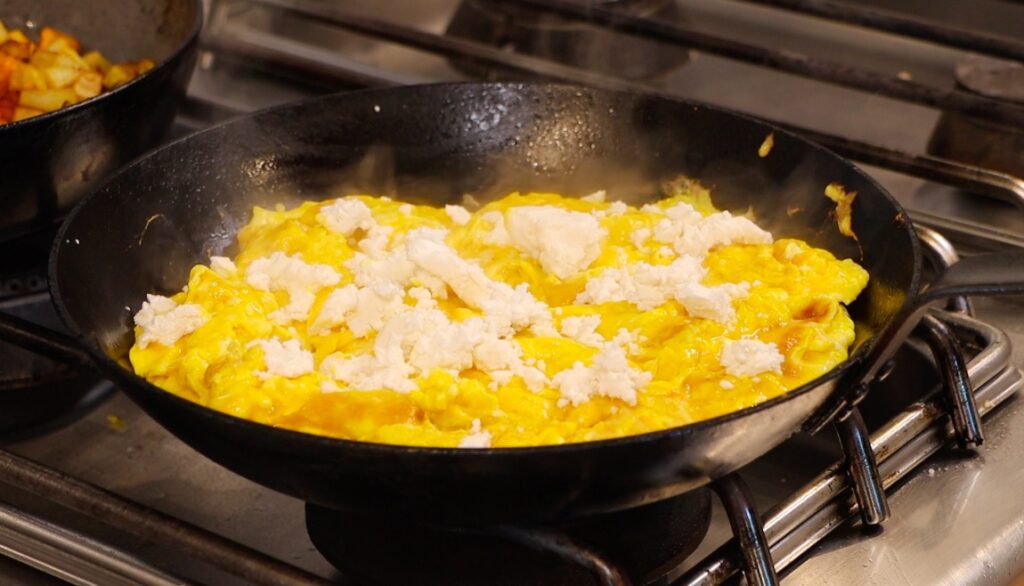 dark yellow omelet in black iron cast pan, steaming, different sized feta crumbs on top