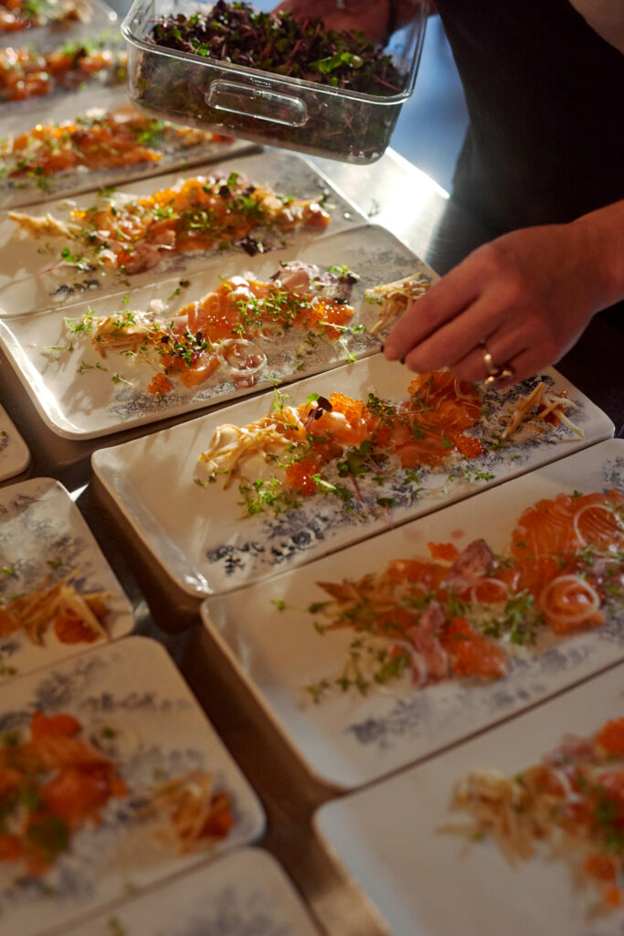 Chef plating cured salmon with roe, herbs and microgreens on ceramic plates
